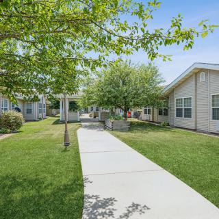 A peaceful outdoor pathway leading between buildings surrounded by trees and grass.