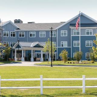 A large blue residential building with a well-maintained lawn and white picket fence, featuring an American flag on display.