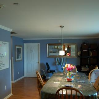 A cozy dining room with a table set and flowers, featuring blue walls, a pendant light, and decor like paintings and a bookshelf.
