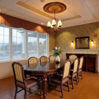 An elegantly designed dining room with a large table and chairs, featuring a chandelier and a window allowing natural light.