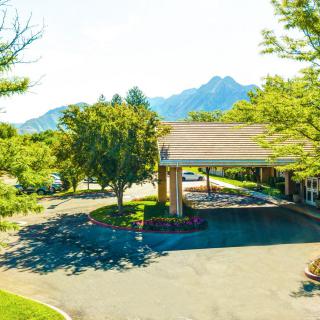 A scenic view of a building entrance surrounded by trees, with mountains in the background on a sunny day.