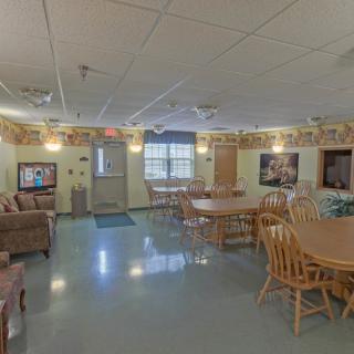A cozy common area with wooden tables, chairs, a sofa, and a television.