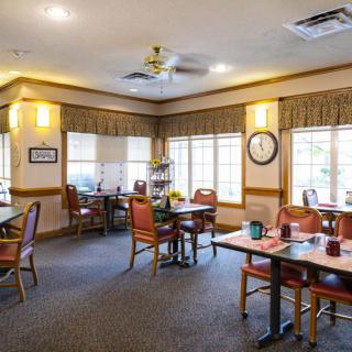A cozy dining area with multiple tables and chairs, featuring large windows and warm lighting.