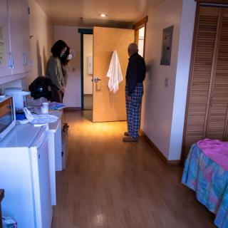 Two people standing in a well-lit room near a doorway.