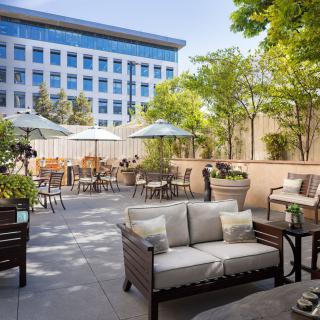 An inviting outdoor patio featuring comfortable seating, tables with umbrellas, and greenery in an urban setting.