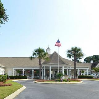 A clubhouse with a circular driveway, featuring palm trees and an American flag at the entrance.