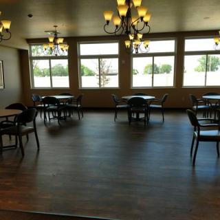 An empty dining room with tables, chairs, and chandeliers, featuring large windows.