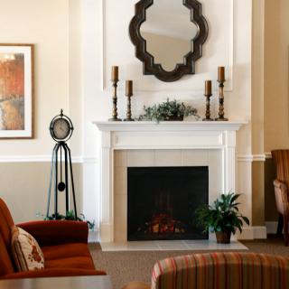 A cozy living room with a central fireplace, adorned with a stylish mirror and candle holders, surrounded by comfortable seating and decorative plants.