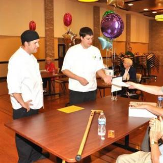 Chefs participate in an indoor event with a judging panel and decorations.
