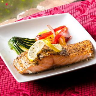 A beautifully plated grilled salmon fillet served with lemon slices and a side of roasted vegetables including zucchini and peppers.
