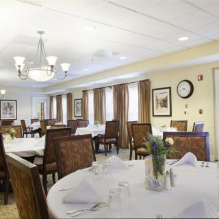 An elegantly decorated dining room with neatly arranged tables and chairs, featuring a chandelier and framed wall art.