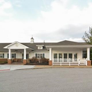 A white single-story building with a driveway and several windows, set against a cloudy sky.