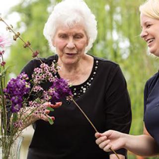 An elderly woman and a younger woman arranging flowers together outdoors.
