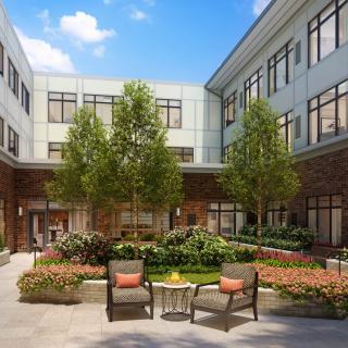 A peaceful courtyard with lush greenery and comfortable seating surrounded by a modern building.