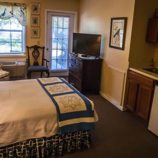 A cozy hotel room with a bed, kitchenette, and a view through large windows.
