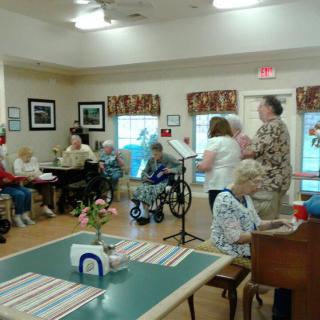 A group of elderly individuals participating in a communal activity at a nursing home, with one person playing the piano.