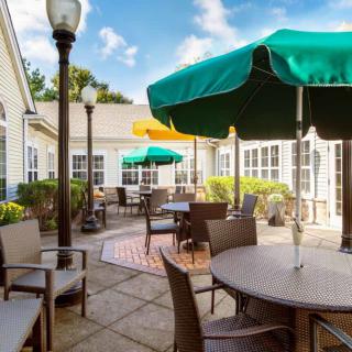 A sunny outdoor patio with several tables and chairs, shaded by green and yellow umbrellas.