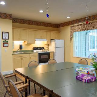 A cozy kitchen and dining area featuring a large table surrounded by chairs, with a stove, refrigerator, and cabinets in the background.