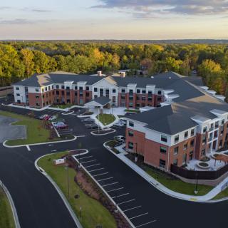 Aerial view of a large residential complex surrounded by trees and a parking lot at sunset.