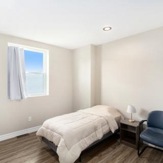 A minimalist bedroom with a single bed, wooden flooring, and ample natural light from the window.