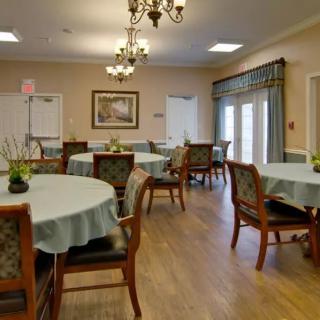 An elegantly decorated dining room with round tables and chairs, featuring chandeliers and light-filled windows.