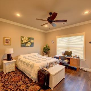 A cozy bedroom with a bed, desk, and ceiling fan, featuring natural lighting and elegant decor.
