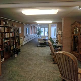 A cozy library room with bookshelves, a seating area, and a large window offering an outdoor view.