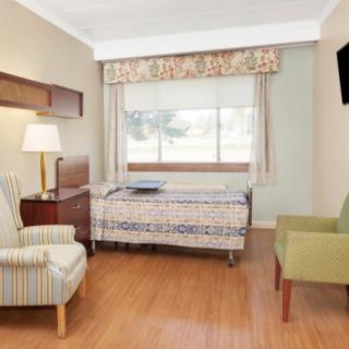 A hospital room with a bed, chairs, and a television.