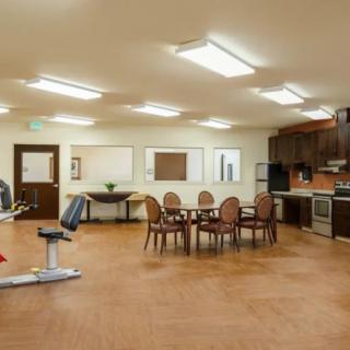 A spacious, well-lit fitness room with exercise equipment and a kitchen area.