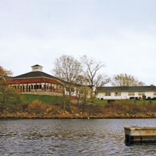 A scenic view of a building by the water's edge with trees in autumn.