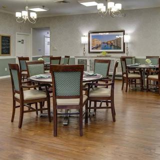 A spacious dining area with neatly arranged tables and chairs, featuring elegant chandeliers and wooden flooring.