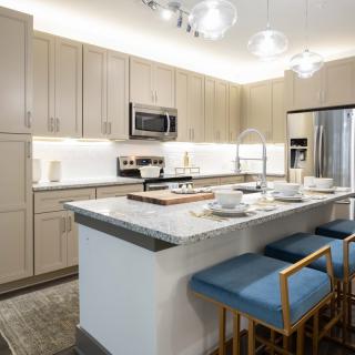 A modern kitchen featuring a central island with blue bar stools, marble countertops, and stainless steel appliances.