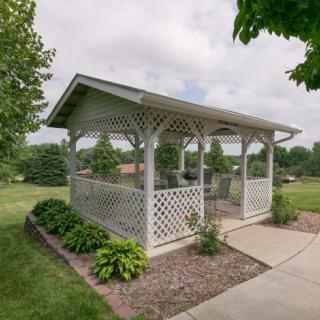 A charming gazebo with latticework and outdoor furniture, set in a lush garden landscape.