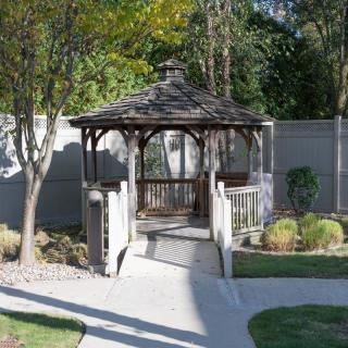 A quaint wooden gazebo surrounded by a landscaped garden with a stone pathway leading to it.