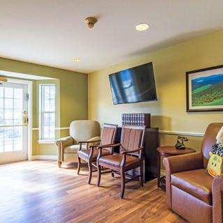 A cozy living room with various chairs, a mounted television, and artwork on the wall.