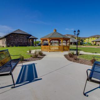 A scenic park area with a central gazebo, surrounded by lawns and benches under a clear blue sky.