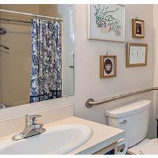 A bathroom with a sink, toilet, and shower area featuring a decorative curtain and wall art.