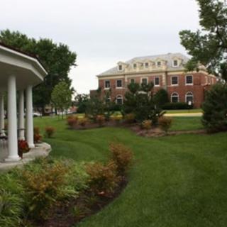 A landscaped garden with a brick building in the background and a columned structure on the left.