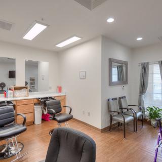 A well-lit hair salon interior featuring stylist stations and a waiting area with chairs and plants.