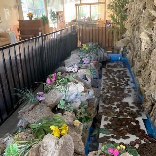 An indoor rock garden with colorful flowers and an artificial pond surrounded by a fence.