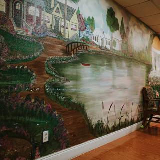 A detailed mural depicting a scenic landscape with houses, a lake, and a winding pathway.