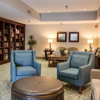 A cozy living room with blue armchairs, a round coffee table, and a bookshelf filled with books.
