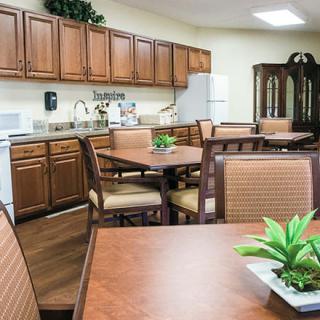 A cozy kitchen and dining area with wooden cabinets, tables, and chairs accented by indoor plants.