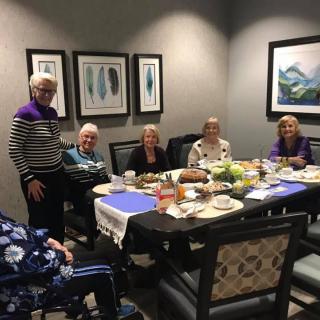 A group of seniors enjoying a meal together at a dining table indoors, surrounded by artwork on the walls.