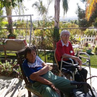 Two elderly individuals sitting outdoors enjoying a sunny day in the garden.