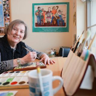 An artist happily engaged in painting at her studio, surrounded by tools and inspiration.