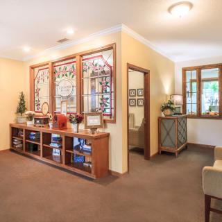 A cozy living room interior featuring a stained glass wall, carpeted floor, and wooden shelving with decorative items.