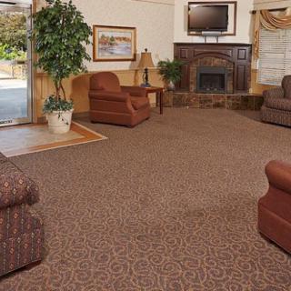 A cozy living room with patterned carpet, comfortable seating, and a fireplace under a mounted television.