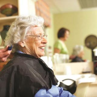 An elderly woman smiles while getting a haircut at a salon.