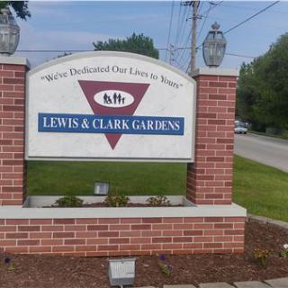 Sign for Lewis & Clark Gardens on a brick base near a street.